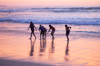Three people walking along the shore at sunset