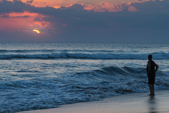 Person standing at water's edge during sunset