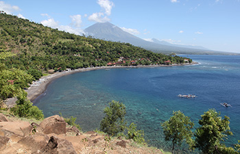 Jemeluk Bay with lush hills, blue sea, and a few houses.