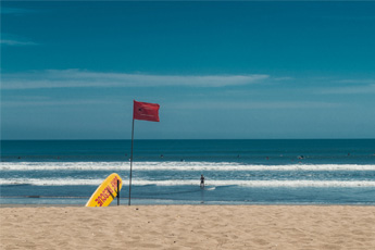 Empty beach with red warning flag in the sand