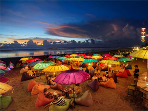 Beach scene lit with glowing umbrellas at night