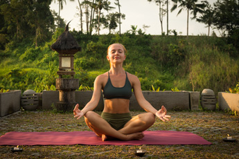 Woman meditating on a yoga mat outdoors at sunrise
